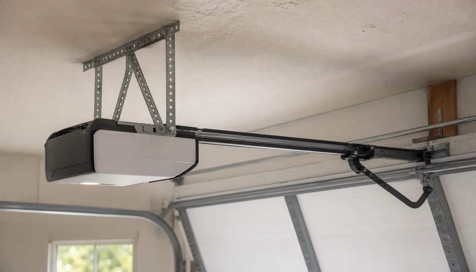 A ceiling-mounted garage door opener motor unit with a rail and trolley running to the top of the door