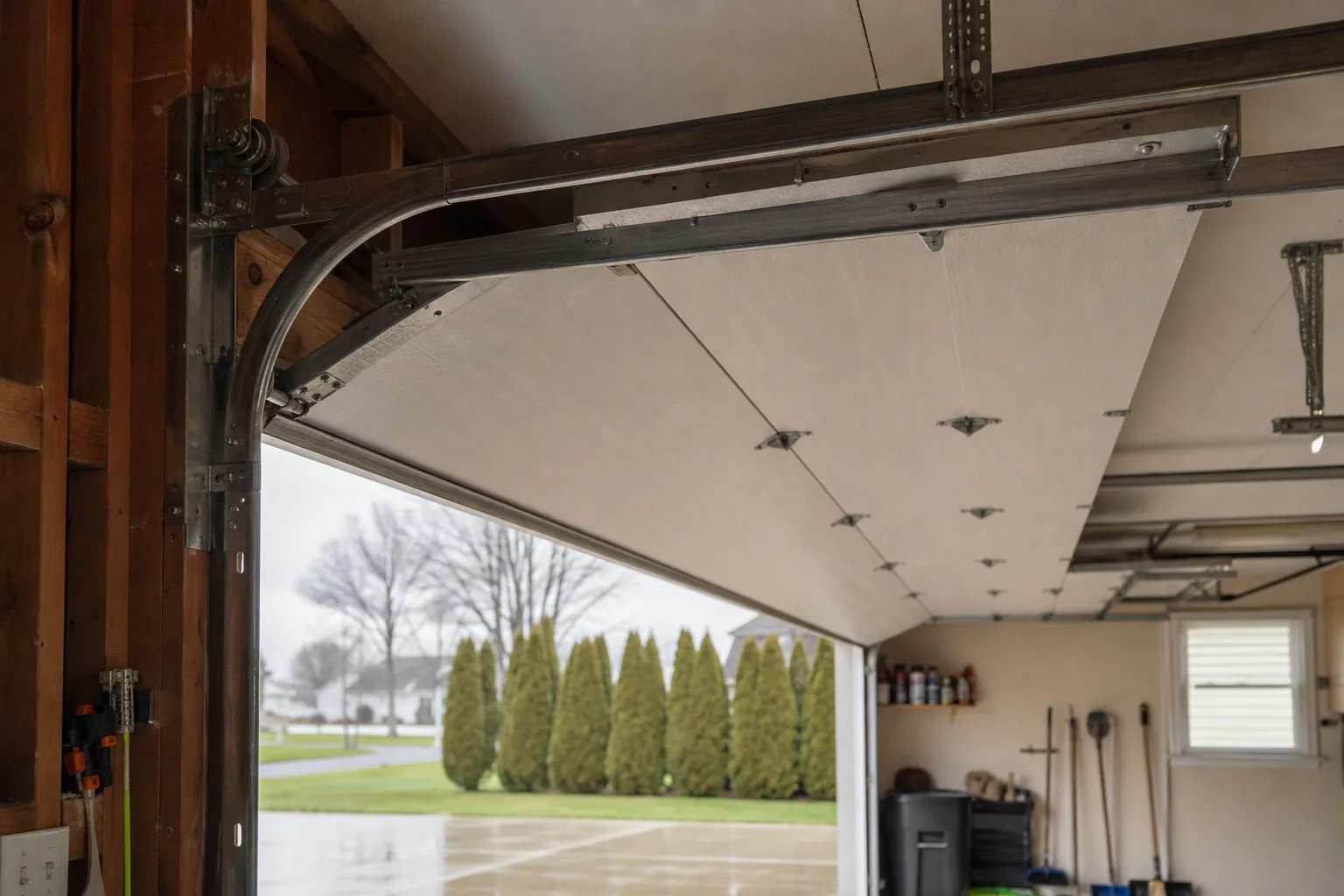 An open residential sectional garage door from inside showing rollers riding in vertical and horizontal steel tracks with panel hinges